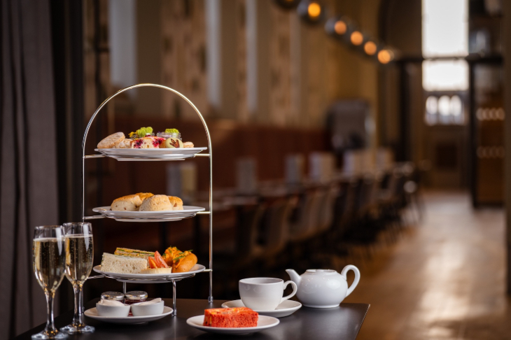 Where to have afternoon tea in London: a three-tiered afternoon tea stand on a table, alongside a teapot, teacup, and glasses of champagne