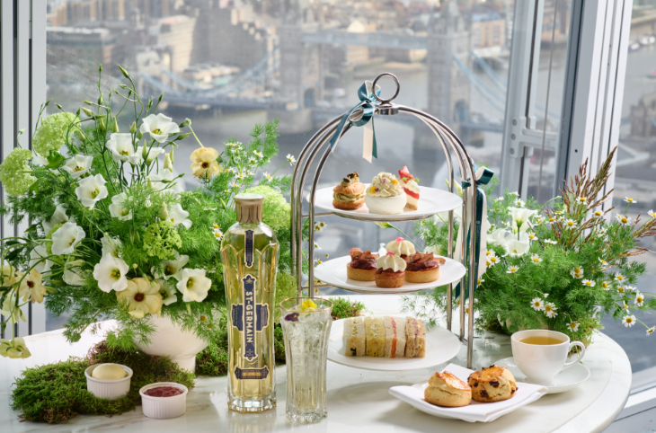 Top afternoon tea in London: a table decorated with greenery, with afternoon tea at the centre. Tower Bridge and the river are visible through the window behind.