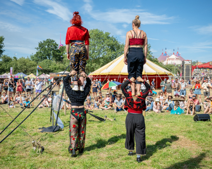 A crowd watching an open-air performance as two people stand on the shoulders of two other people