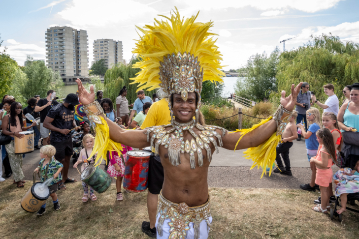 A person in a Carnival-style costume including feathered head dress in front of a crowd in a park