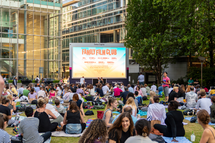 People sitting on grass in front of a large open air cinema screen