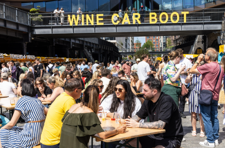 Things to do in London this weekend: people sitting and standing around picnic tables in Coal Drops Yard, beneath a 'Wine Car Boot' sign