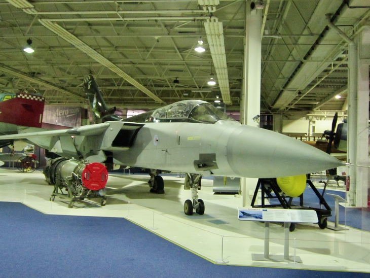 A grey Panavia Tornado F3 fighter jet on display in a museum hangar, with its engine and nose cone shown separately on stands.
