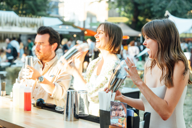 Three people standing in a row at a bar shaking cocktail shakers