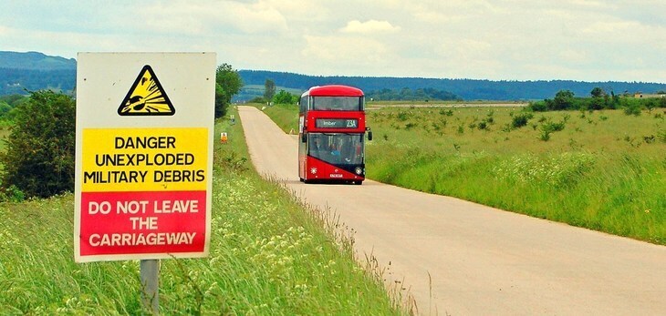 Things to do in London today: a red London double-decker Routemaster driving along a road in the countryside, in front of a sign warning of unexploded military debris