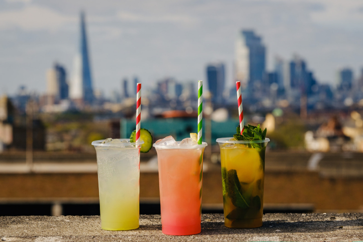 Three colourful cocktails on a wall, with the London skyline in the background
