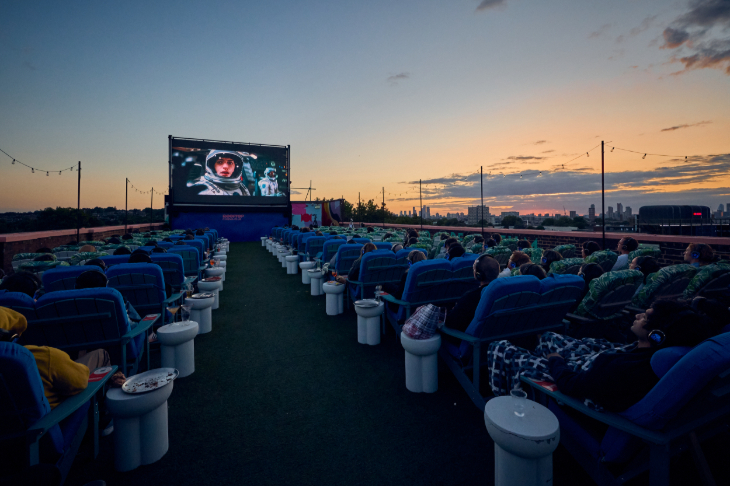 People watching a film on a large screen at an open-air rooftop cinema