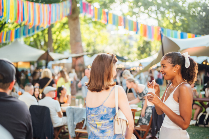 August 2026 in London: people sitting and standing around with drinks, beneath fairy lights and colourful bunting in a garden