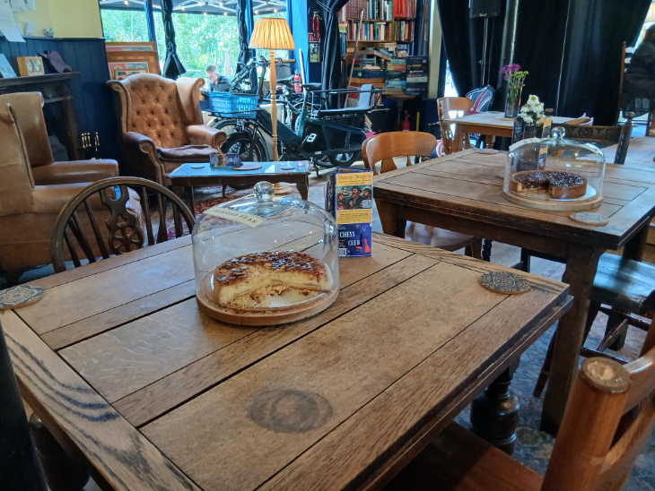 طاولات خشبية في مسرح Tea House، تحتوي كل واحدة منها على علبة كعكة ذات قبة زجاجية تحتوي على طبقة من الكعك