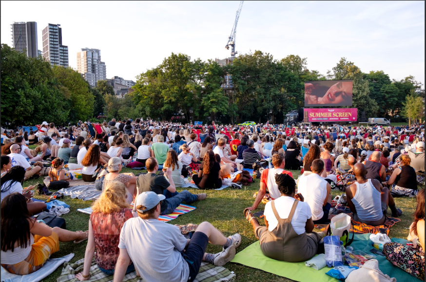 People sitting on picnic blankets on grass watching an open-air cinema screen