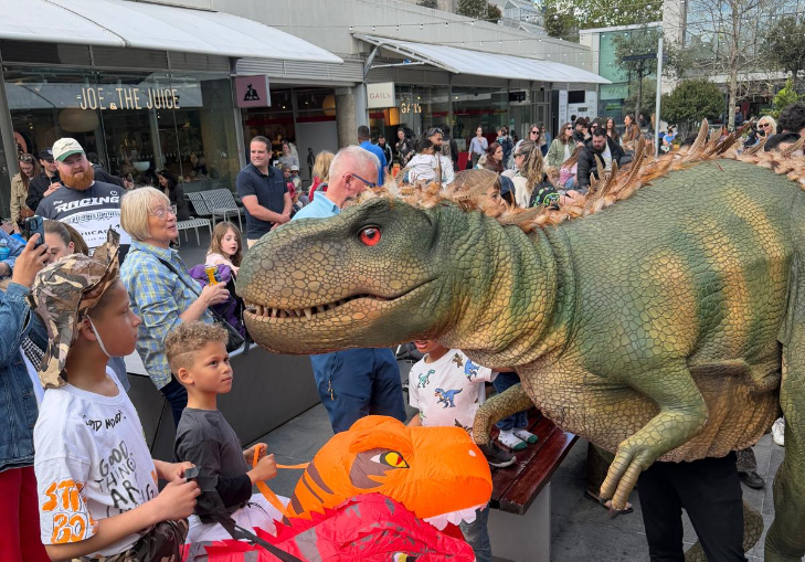 People getting up close to a large dinosaur puppet