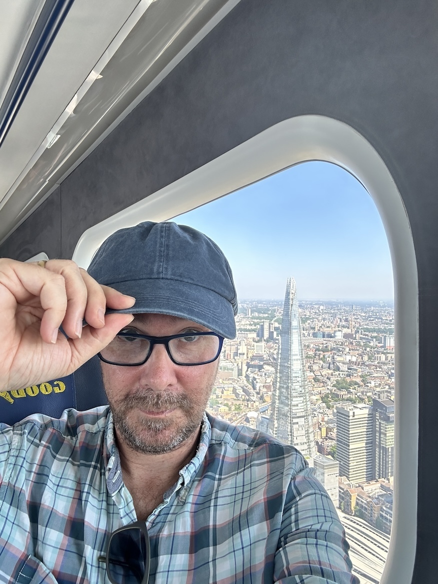 Matt Brown of Londonist doffs his cap from the Goodyear Blimp, with the Shard behind