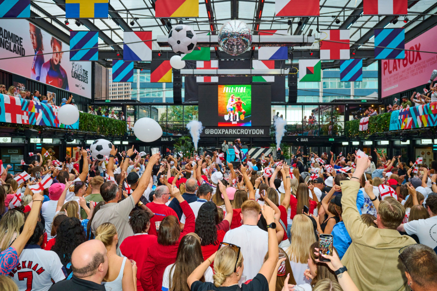 Things to do in London today: crowds watching football on a large screen at Boxpark, beneath the flags of several countries
