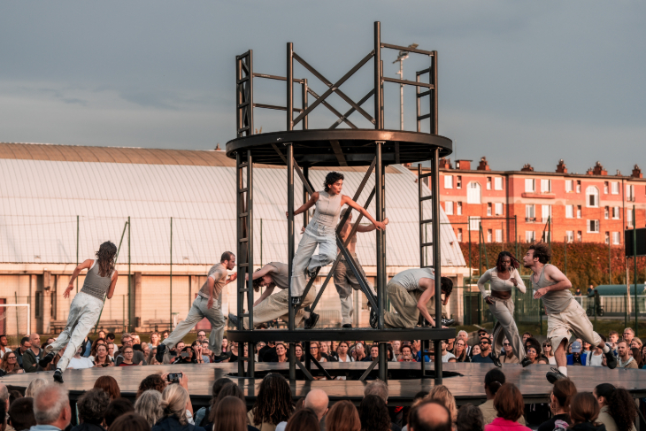 August 2026 in London: dancers performing on a circular open-air stage made of ladders, watched by a crowd