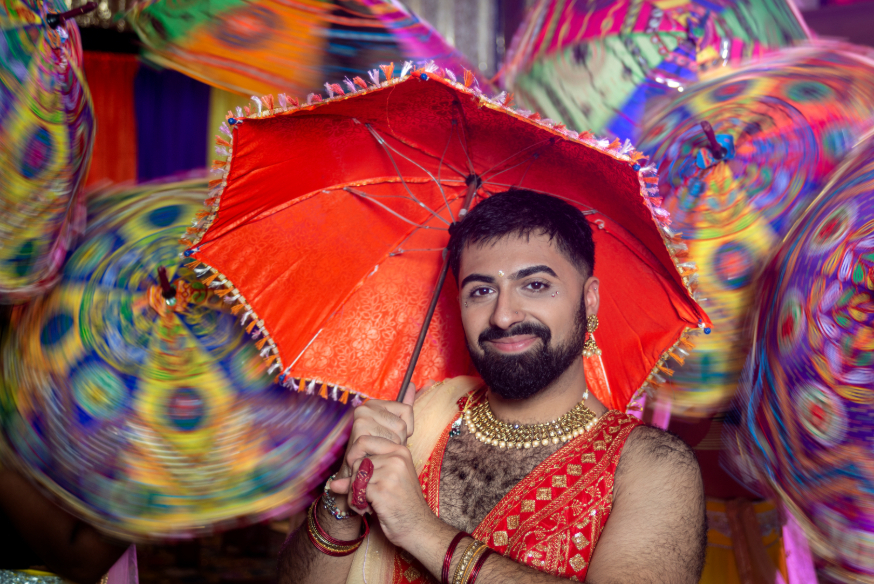 A person in red Indian-inspired costume with gold jewellery, holding a red umbrella