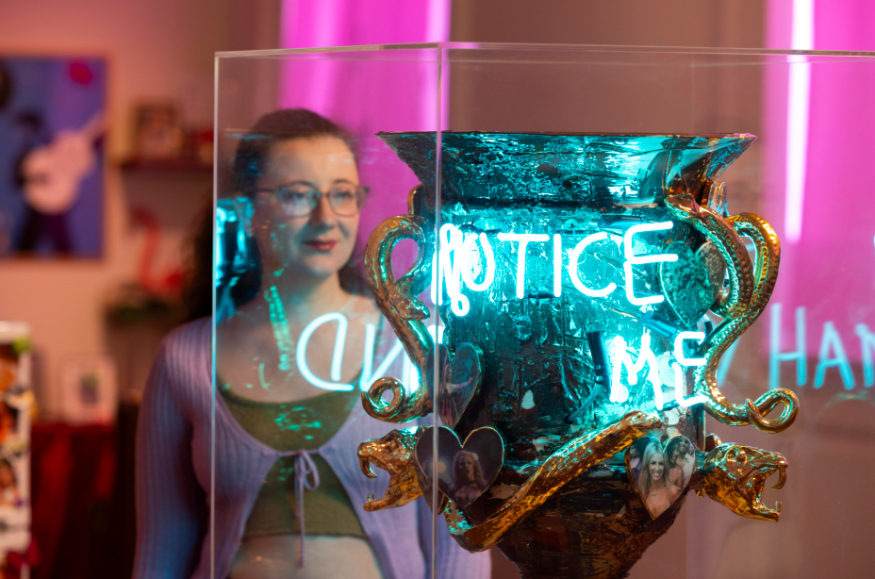 A woman looking at an urn in a glass display case, with blue neon lights reflected from nearby