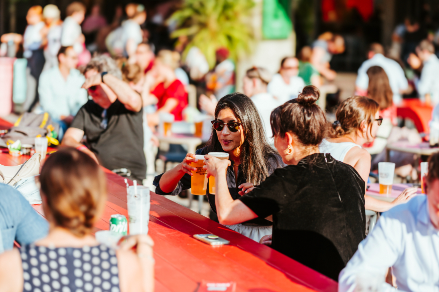 People sitting at a picnic table in the sun, holding pints of beer