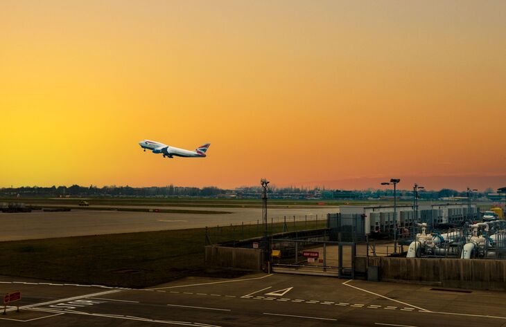 A British Airways Boeing 747 takes off from an airport runway into a vibrant orange and yellow sunset sky.
