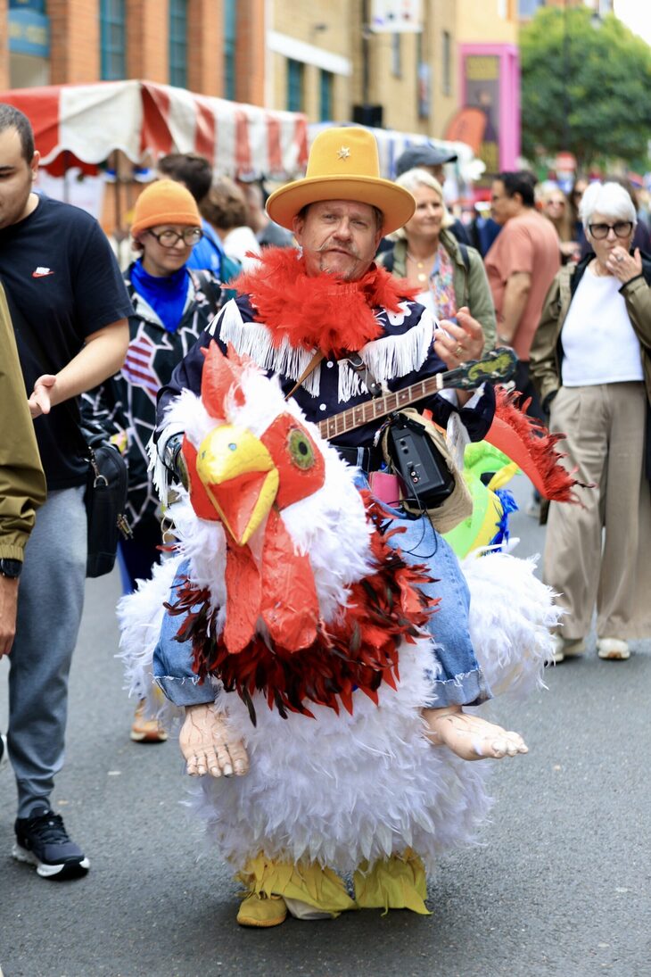 A man 'riding' a chicken, playing a banjo