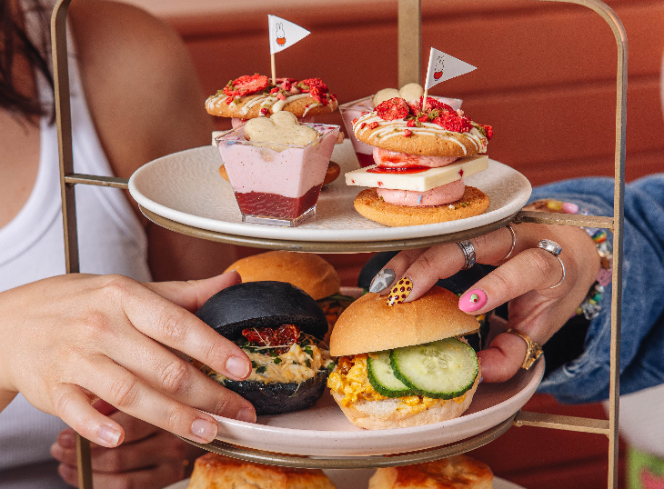 Best budget afternoon tea London: two hands reaching for rolls on a three-tiered afternoon tea stand