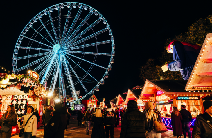 Hyde Park Winter Wonderland Christmas 2026 guide: the big wheel and wooden cabins at the Christmas market, illuminated at night