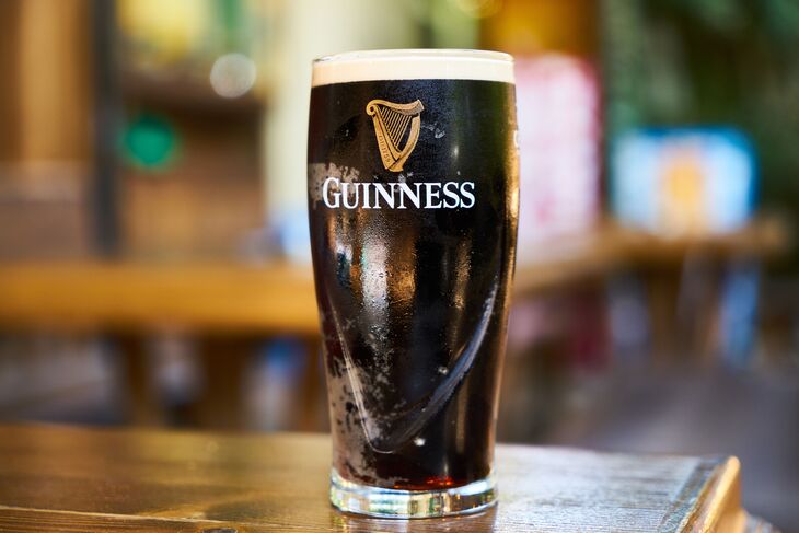A pint of dark Guinness stout with a thick white head in a branded glass, sitting on a wooden bar top.