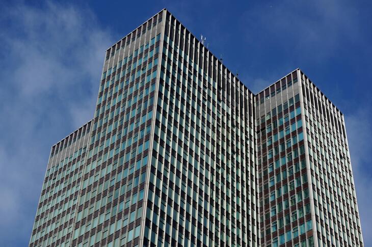 Low-angle view of a tall, modern skyscraper with a grid-like facade of windows and vertical metal beams against a blue sky with light clouds.