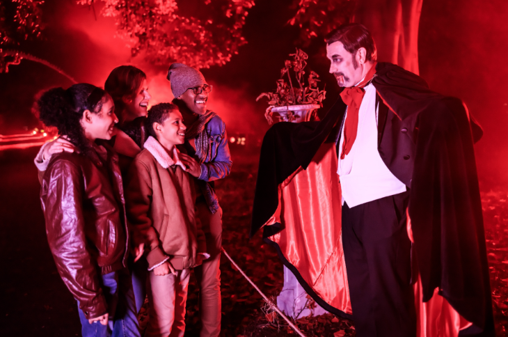 October 2026 half term in London: a family of four in conversation with somebody dressed as a vampire, among a red-lit garden at night