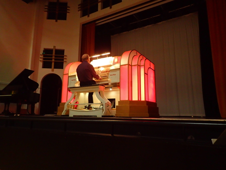 Halloween 2026 film screenings London: A man plays a large, illuminated Wurlitzer theatre organ on a stage, flanked by a grand piano and red curtains.