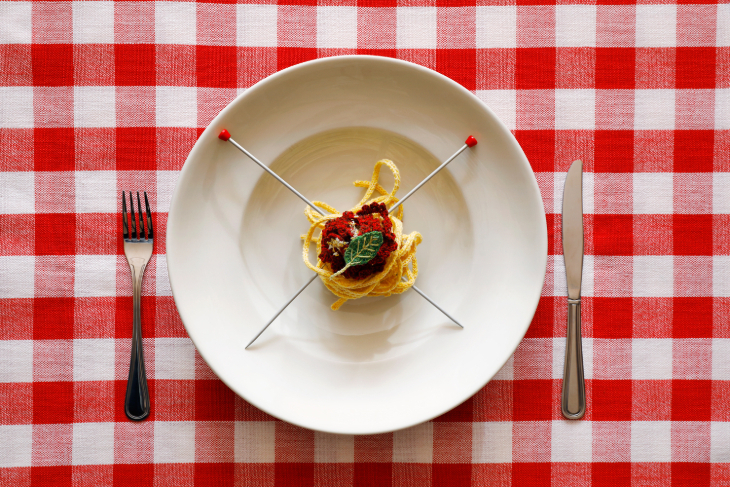 A plate of spaghetti, except the spaghetti is strands of yellow wool, with two knitting needles through the centre