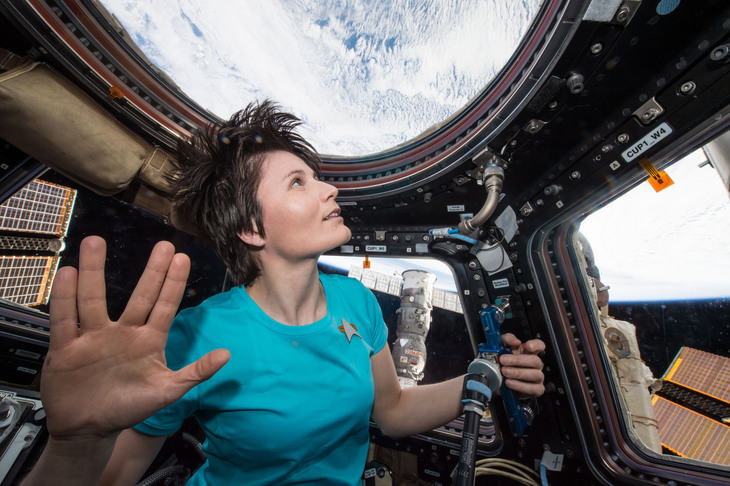 Astronaut Samantha Cristoforetti in the ISS Cupola, wearing a Star Trek uniform and giving the Vulcan salute with Earth visible through the windows.
