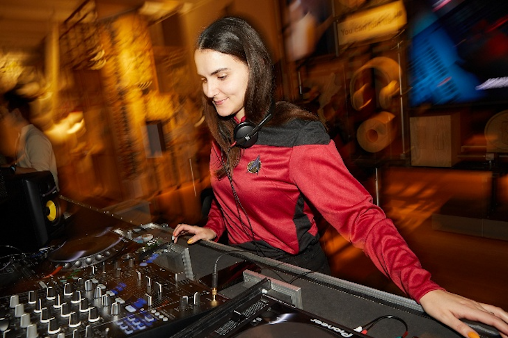 A lady in a counterfeit Star Trek command uniform operates a DJ deck