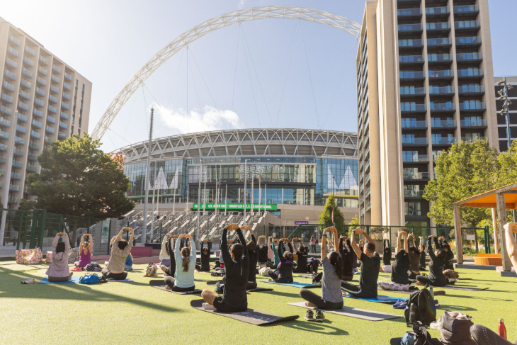 Things to do in London today: people taking part in a yoga session on grass in front of Wembley Stadium