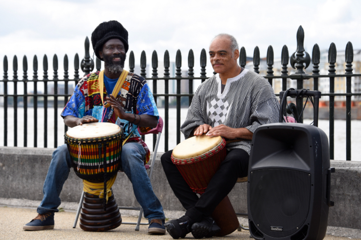 Things to do in London this weekend: two people sitting on a wall in front of the Thames, drumming