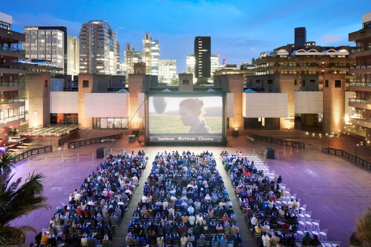 What's on in London today: people sitting in rows of chairs in front of a large cinema screen, in an open-air courtyard at Barbican