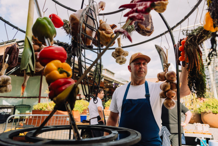 Things to do in London today: a chef in front of a fire pit, framed by strings of vegetables and herbs hanging from above