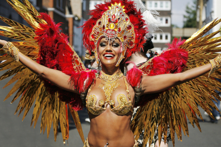 A dancer with her arms outstretched in a red and gold carnival costume