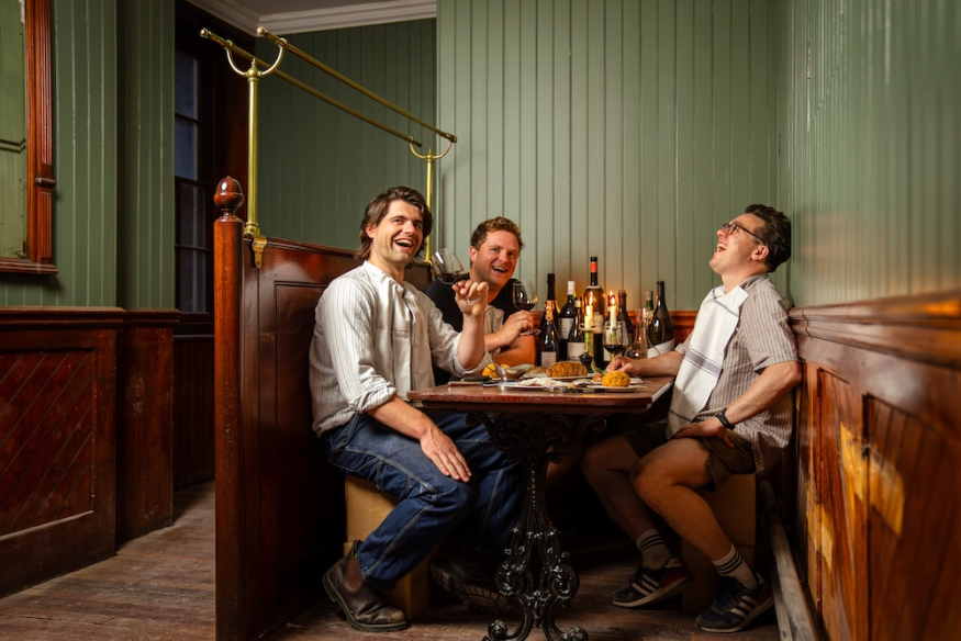 Three men sitting in a booth with a table full of drinks bottles