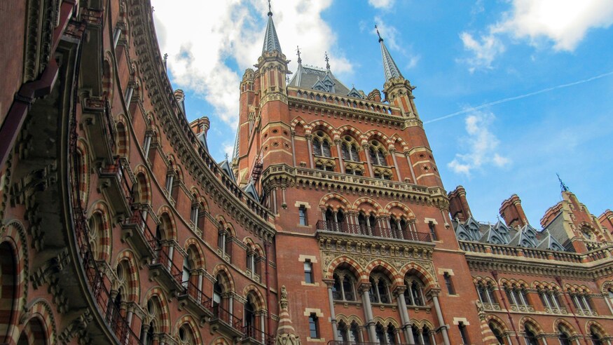 Low-angle view of the ornate red brick Gothic Revival facade of St. Pancras International station in London against a blue sky.
