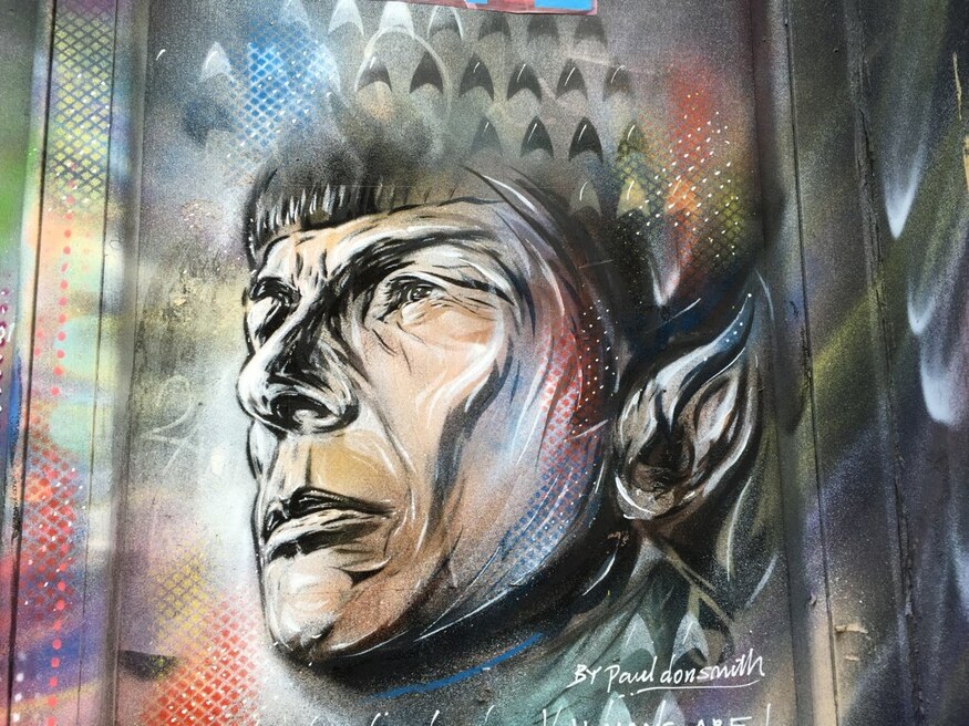 Graffiti portrait of Spock from Star Trek, featuring his iconic pointed ear and bowl haircut, rendered in a stylized spray-paint aesthetic with colorful stenciled patterns.