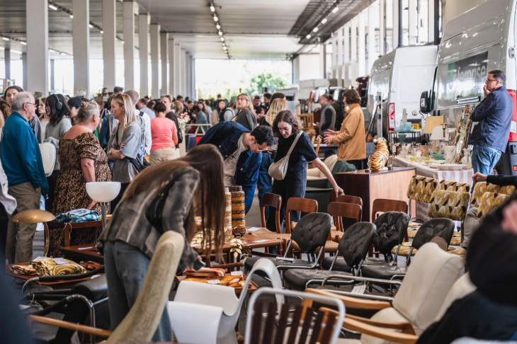 Things to do in London this weekend: crowds of people at a covered flea market. The stall at the forefront of the photo is selling many chairs