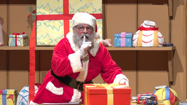 Family Christmas theatre shows 2026: Santa in a workshop surrounded by gifts, with a finger to his lips in a "sshhhh" motion