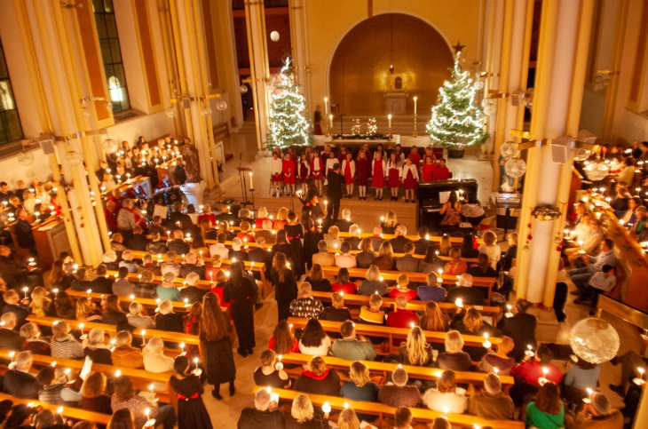 Christmas carol concerts London 2026: a choir performing in church in front of an audience, who are seated in pews, each holding a candle