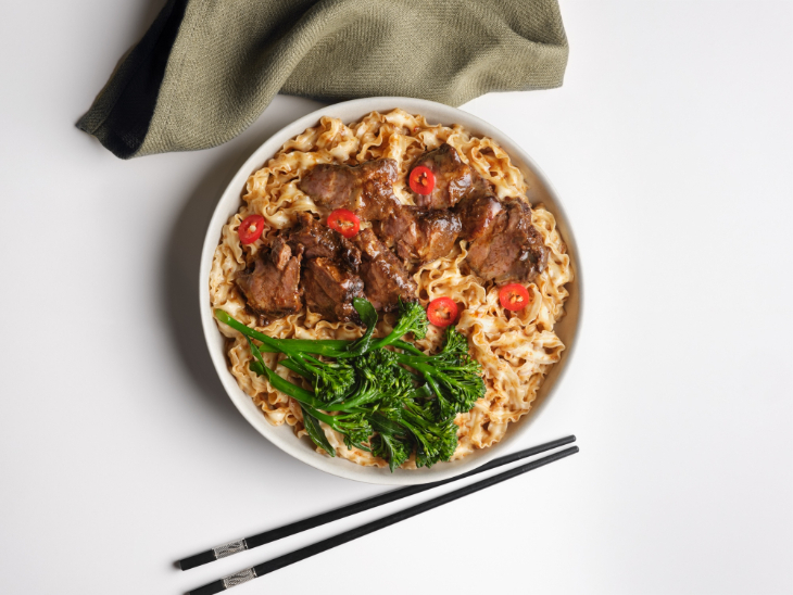 A bowl of noodles topped with beef, vegetables and sliced chillis