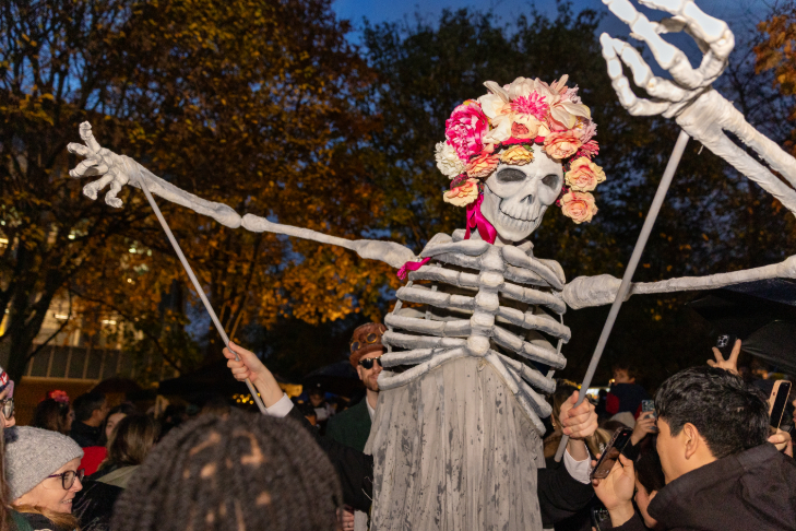 Halloween 2026 parties London: a larger than life skeleton puppet wearing a pink flower crown being moved through a crowd of people at dusk