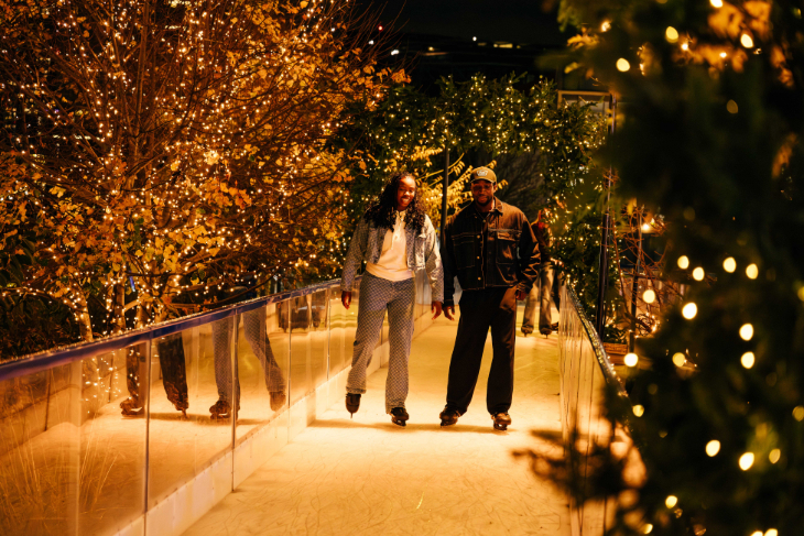 Christmas 2026 ice rinks in London: a couple skating side by side along an ice rink path, surrounded by twinkly trees
