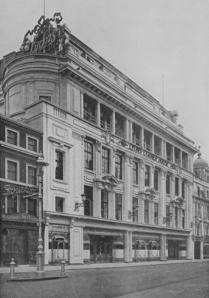 A black-and-white historical photograph of the Lyons' Corner House in London, a grand multi-story building with classical architectural details, large windows, and a prominent rooftop sign. A street lamp and a neighboring shop for Waterman's Ideal Fountain Pens are visible in the foreground.