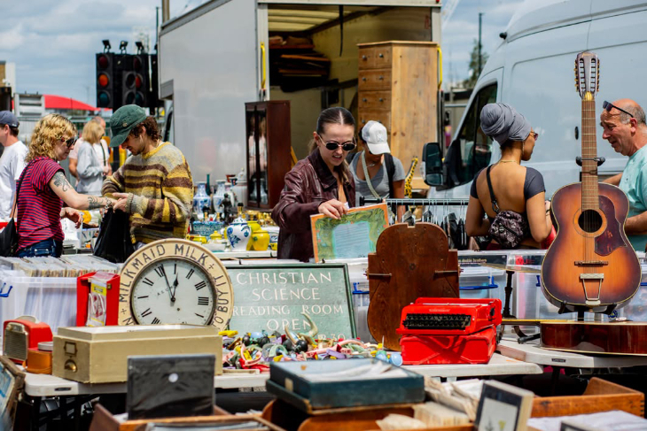 Things to do in London this weekend: people browsing an open air flea market, with a guitar, a clock, signs, and a typewriter among the items displayed on tables