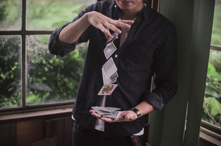 Things to do in London today: A person in a dark button-down shirt performs a card trick, cascading a stream of playing cards from their top hand into their bottom hand.