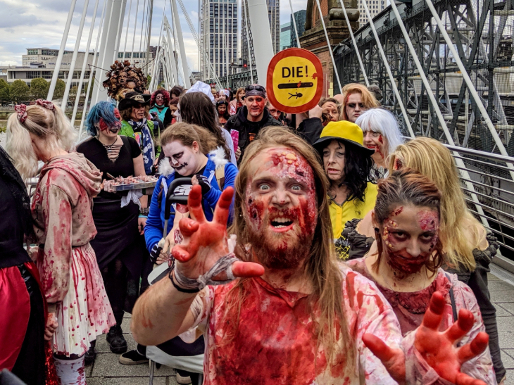 A group of people dressed as zombies, some covered in blood, on Hungerford Bridge over the Thames